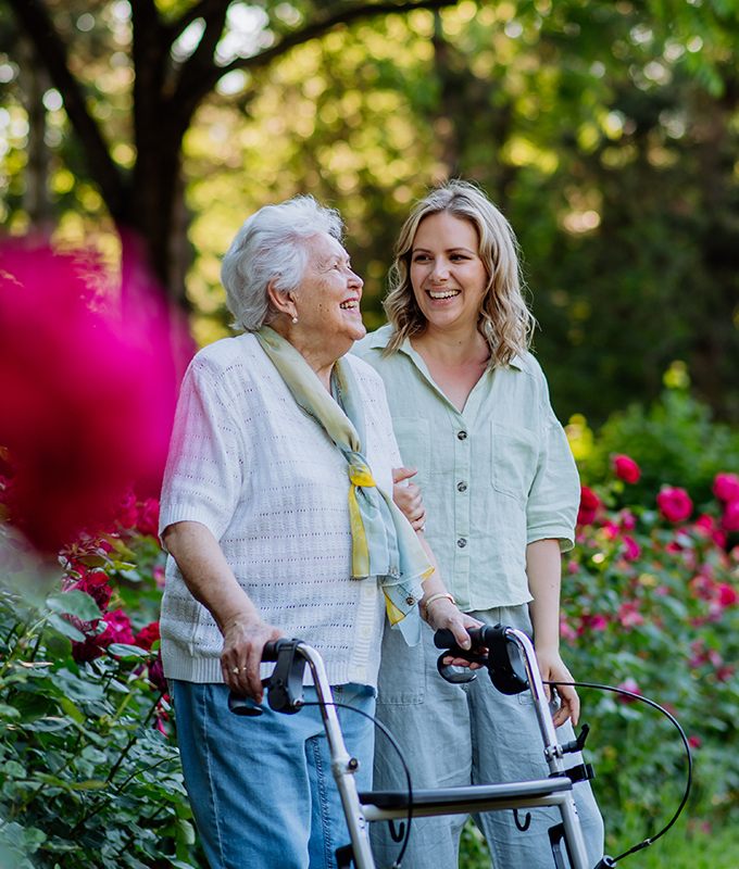 a lady and an elderly woman taking a walk through a flowerbed of roses